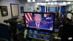President Donald Trump is seen on monitors in the briefing room of the White House, as he gives a prime-time address in the Oval Office, Jan. 8, 2019.