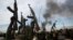 FILE - Rebel fighters hold up their rifles as they walk in front of a bushfire in a rebel-controlled territory in Upper Nile state, South Sudan Feb. 13, 2014. 