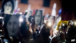 File - People hold pictures of journalist Daphne Caruana Galizia, who was slain in October 2017, as they protest in Valletta, Malta, Nov. 29, 2019.