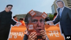 A protester wearing a mask of U.S. President Donald Trump performs with cut-out photos of North Korean leader Kim Jong Un and South Korean President Moon Jae-in, right, during a rally in Seoul, South Korea, May 25, 2018. 