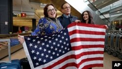 Jayne Novak, izquierda, junto a su esposo, Allen Novak, tras llegar de Irán, y su hija Nikta, posan con una bandera estadounidense en el aeropuerto internacional de Seattle, Washington, el lunes, 6 de febrero, de 2017.