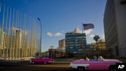 FILE - Tourists ride in classic American convertible cars past the United States embassy, right, in Havana, Cuba, Jan. 12, 2017.