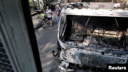 People walk between burnt-out vehicles at the site of recent clashes between anti-government protesters and police near the Government house in Bangkok, Thailand, Dec. 7, 2013. 