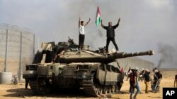 ARCHIVO - Los palestinos ondean su bandera nacional y celebran junto a un tanque israelí destruido en la valla del sur de la Franja de Gaza, al este de Khan Younis, el sábado 7 de octubre de 2023, el día de los ataques de Hamás contra Israel.