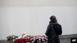(File) A woman pays tribute in front of a wreath of flowers, outside the satirical newspaper Charlie Hebdo's former office, after a ceremony marking the fifth anniversary of the attack in Paris, Jan. 7, 2019. 