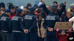 A migrant girl holds a banner as migrants stand at a road blockade near the border crossing with Croatia, in Maljevac, Bosnia, Oct. 24, 2018.