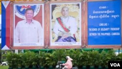 ប្រជាពលរដ្ឋម្នាក់ជិះកាត់ការតុបតែងរូបថតដើម្បីទទួលទស្សនកិច្ចផ្លូវរដ្ឋនៃប្រធានាធិបតីហ្វីលីពីនលោក រ៉ូឌ្រីហ្គូ ឌើទើតេ (Rodrigo Duterte) (រូបឆ្វេង) និងព្រះមហាក្សត្រកម្ពូជាព្រះករុណាព្រះបាទនរោត្តម សីហមុនី (រូបស្ដាំ) នៅរវាងមហាវិថីសុធារស និងមហាវិថីព្រះសីហនុ នៅថ្ងៃច័ន្ទ ទី១២ ខែធ្នូ ឆ្នាំ២០១៦ នារាជធានីភ្នំពេញ។ (ឡេង ឡែន/VOA) 