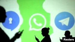 Des silhouettes d'utilisateurs mobiles sont visibles à côté des logos des applications de médias sociaux Signal, Whatsapp et Telegram projetés sur un écran.