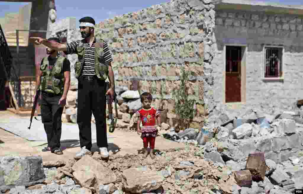 A Syrian child stands next to rebel fighters checking a house that was damaged in bombing by government forces in Marea, on the outskirts of Aleppo, Syria, September 4, 2012. 