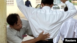 FILE - A Cambodian school security official searches a student for exam 'cheat sheets' at the gates of a school in Phnom Penh.