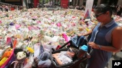 A woman pushes a pram past a temporary memorial site close to the Lindt cafe in the central business district of Sydney, Australia, where people continue to stream past to leave floral tributes Thursday, Dec. 18, 2014. 