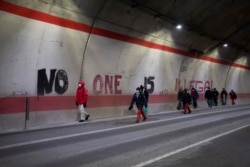 Migrants headed to France from Italy walk past graffiti that reads "No One is Illegal" in a tunnel leading to the French-Italian border, Saturday, Dec. 11, 2021.