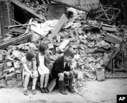 In this photo provided by the U.S. Office of War Information, three children are sitting next to the remains of what was once their home in East London after another night of German bombings, in the early days of the Blitz during World War II, September 1940.