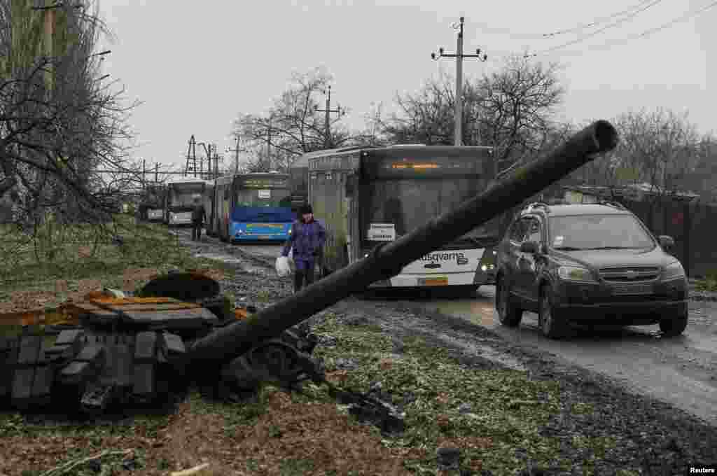Empty buses wait along a road beside a burned-out tank turret while traveling in the direction of Debaltseve to evacuate the residents, in Vuhlehirsk, Donetsk region, Feb. 6, 2015.