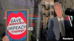 FILE - An opponent of U.S. President Donald Trump carries a sign about impeachment next to a supporter with a cardboard cutout in Boston, Jan. 19, 2019.