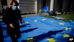 FILE - A man with a face mask and a child with an EU flag are seen at an event to garner more support for Italy during the coronavirus pandemic, in front of the Italian Embassy in Berlin, Germany, April 22, 2020.