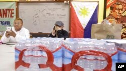 Terrence Valen, president of the National Alliance for Filipino Concerns, center, talks on the phone next to Joey Elacion as they sit behind bottles of water donated by Elacion for victims of Typhoon Haiyan, at the Filipino Community Center in San Francisco, Nov. 11, 2013. 
