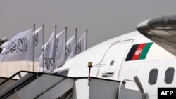 An aircraft with Afghanistan's flag is seen in front of Taliban flags fluttering on poles at the airport in Kabul, Sept. 11, 2021.