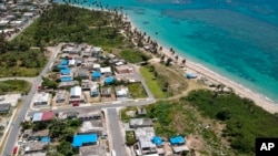 FILE - An aerial photo shows the Viequez neighborhood, east of San Juan, Puerto Rico, where people were still living in damaged homes, protected by blue plastic tarps, months since Hurricane Maria devastated the island, June 18, 2018. 