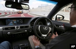 FILE - An employee of Toyota Motor Corp. sits behind the steering wheel of a self-driving vehicle during a test drive in Tokyo.