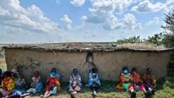 Des artistes culturels de la tribu Masaï, portant des masques en tissu, s'abritent à l'ombre d'un abri traditionnel entouré de bouse de vache dans leur village de Talek, dans la réserve nationale du Masai Mara, comté de Narok, Kenya, le 24 juin 2020.