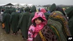 A migrant holds her child as she queues for food portions at the Greek border camp near Idomeni, March 10, 2016. 