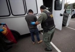 FILE - An U.S. Immigration and Customs Enforcement officer transfers a man in hand and ankle cuffs onto a van during an operation in Escondido, Calif., July 8, 2019.