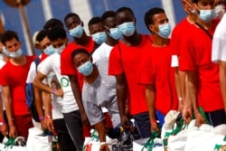 FILE - Migrants queue to embark on a ferry to the mainland, in the Sicilian island of Lampedusa, Italy, June 23, 2021.