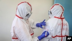 FILE - A nurse writes on the protective clothing of fellow nurse Lucy Kanyi, right, with her name so she can be recognized when wearing it and the time of day, at the infectious disease unit of Kenyatta National Hospital, Nairobi, Kenya, March 6, 2020.