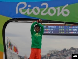 FILE - Silver medalist Feyisa Lilesa of Ethiopia crosses his wrists as he celebrates on the podium after the men's marathon at the 2016 Summer Olympics in Rio de Janeiro, Brazil, Aug. 21, 2016. He had made the same gesture of protest as he approached the finish line of the race.