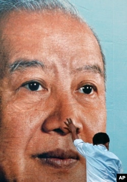 A man holds a portrait of former King Norodom Sihanouk as he and other workers try to hang it on the facade of the Royal Palace in Phnom Penh, Cambodia, as part of preparations for his funeral, October 16, 2012.