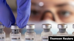 FILE - A woman holds vials labelled "COVID-19 Coronavirus Vaccine" over dry ice in this illustration created December 5, 2020.