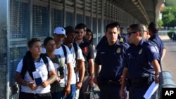 FILE - U.S. Customs and Border Patrol officers are seen with asylum-seekers on the international bridge between Laredo, Texas, and Nuevo Laredo, Mexico, July 10, 2019.