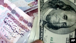 FILE - A man displays a 100 U.S. dollar and 50 Egyptian pound notes in Cairo. 