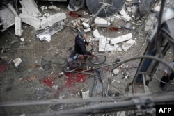 A Syrian man walks with a bicycle amid the rubble of destroyed buildings following a reported air strike by Syrian government forces in the rebel-held area of Douma, east of the capital Damascus, on Oct. 29, 2015.