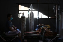 Seorang pasien COVID-19 duduk di atas velbed di tenda sementara di luar ruang gawat darurat rumah sakit pemerintah di Bekasi, 25 Juni 2021. (Foto: REUTERS/Willy Kurniawan)