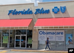 FILE - A person walks by a health care insurance office in Hialeah, Fla.