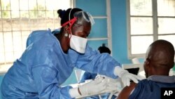 A health care worker from the World Health Organization, left, gives an Ebola vaccination to a front line aid worker who will then vaccinate people who might potentially have the virus, in Mbandaka, Congo, May 30, 2018.