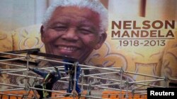 An image of Nelson Mandela is displayed on a digital screen as workers on scaffolding construct a stage ahead of Mandela's national memorial service at First National Bank (FNB) Stadium, also known as Soccer City, in Johannesburg, Dec. 9, 2013.