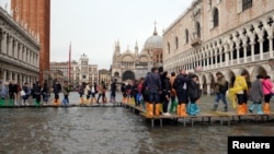 People walk on a catwalk in a flooded Saint Mark Square during a period of seasonal high water in Venice, Italy, Oct. 29, 2018 
