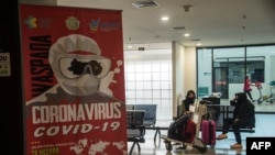 Women sit near a COVID-19 sign in a departure terminal at Juanda international airport in Surabaya, East Java, on April 24, 2020.