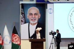 Backdropped by his own image, Afghan President Ashraf Ghani speaks to delegates during the first day of the Afghan Loya Jirga meeting in Kabul, Afghanistan, April 29, 2019.