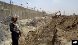 FILE - A Pakistani border guard watches as an excavator digs a trench along Pakistan's border with Afghanistan, at Chaman post in Pakistan, May, 16, 2014.