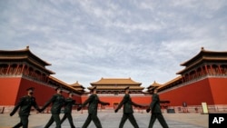 FILE - Soldiers wearing protective face masks march past the closed entrance gates to the Forbidden City, usually crowded with tourists before the coronavirus outbreak in Beijing, March 12, 2020.