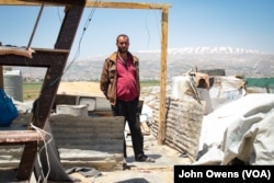 Hussein Muhammed Michel stands among his family's possessions. They have moved the items outside the home in anticipation of a move, but have not yet found a site to move to.