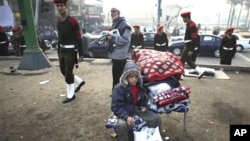 A boy waits with his belonging as Egyptian officers walk behind him, in Tahrir Square, in Cairo, Egypt, February 14, 2011