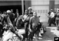 Rev. Ralph Abernathy and Martin Luther King, Jr., are taken by a policeman as they led a line of demonstrators into the business section of Birmingham, Alabama, April 12, 1963.