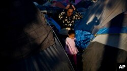 A woman and a girl who traveled a caravan of migrants walks between tents at the Benito Juarez Sports Center which is serving as a shelter in Tijuana, Mexico, Nov. 26, 2018.