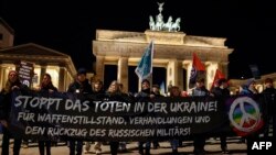 Мітингувальники з гаслом "Зупиніть вбивства в Україні! За припинення вогню, переговори та виведення російських військ!" перед Бранденбурзькими воротами у Берліні 23 лютого 2024 р. Фото: Odd Andersen/AFP