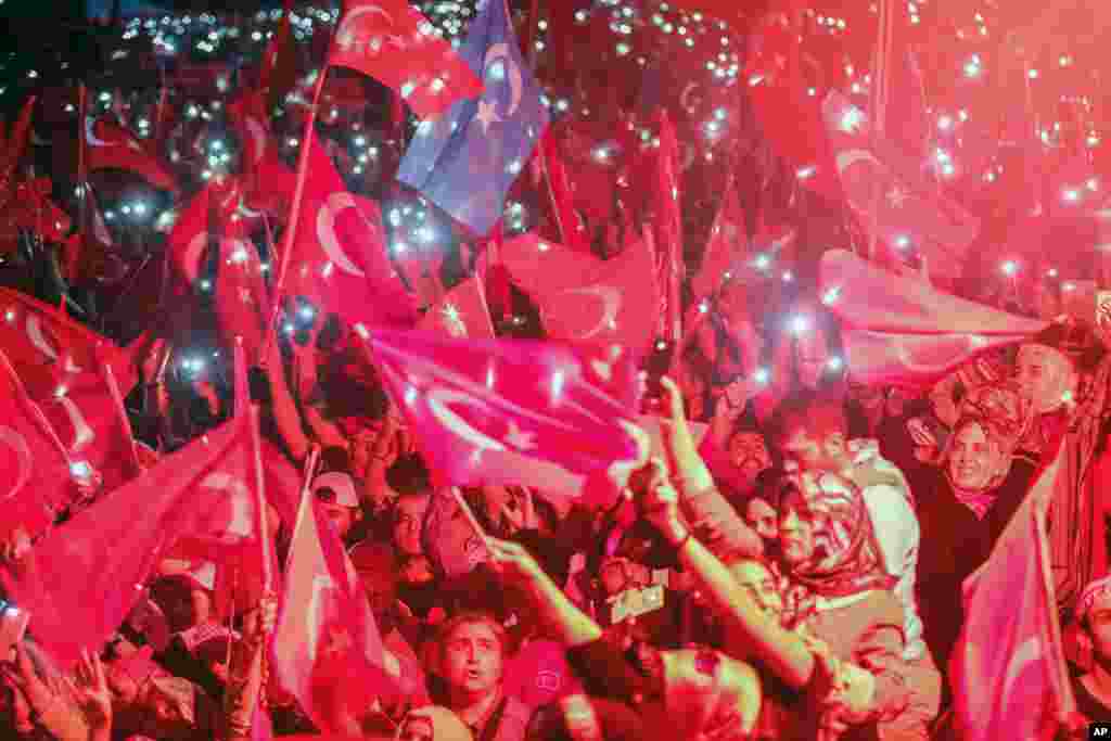 Turkish people wave flags of their country and use the lights of their cell phones during the speech of President Recep Tayyip Erdogan in Istanbul, Aug. 7, 2016.